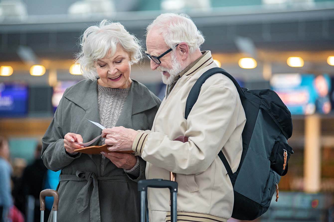 Older couple stands in airport terminal holding flight tickets