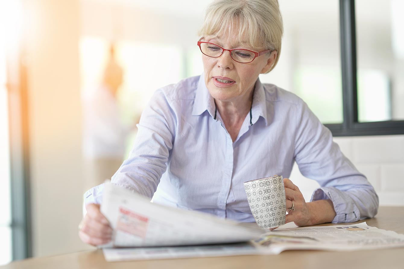 Senior woman with eyeglasses reading newspaper at home