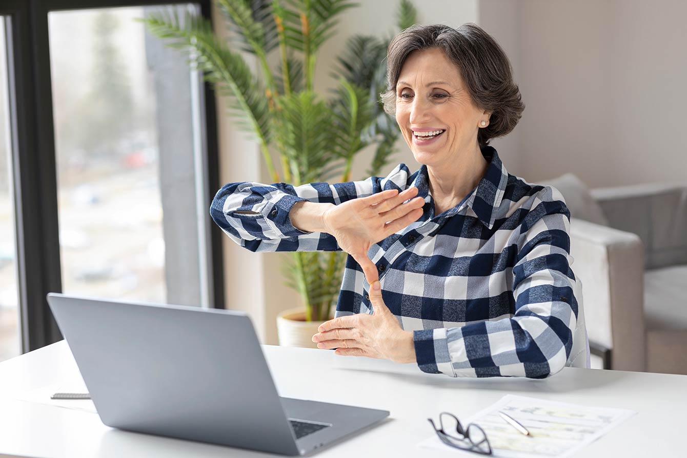 Happy deaf elderly woman uses sign language while video call using laptop