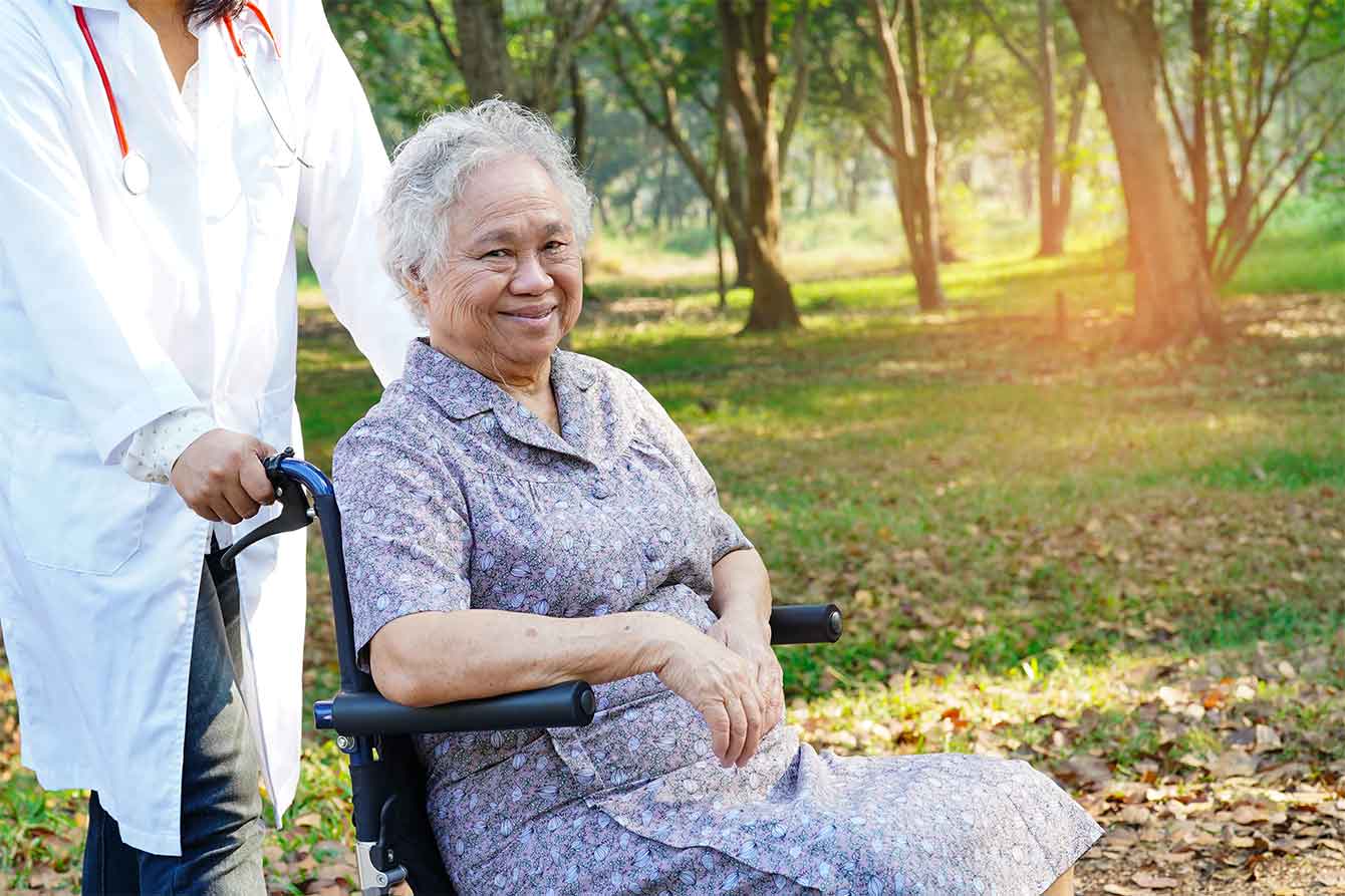 Asian senior in wheelchair smiles during a beautiful day in the park