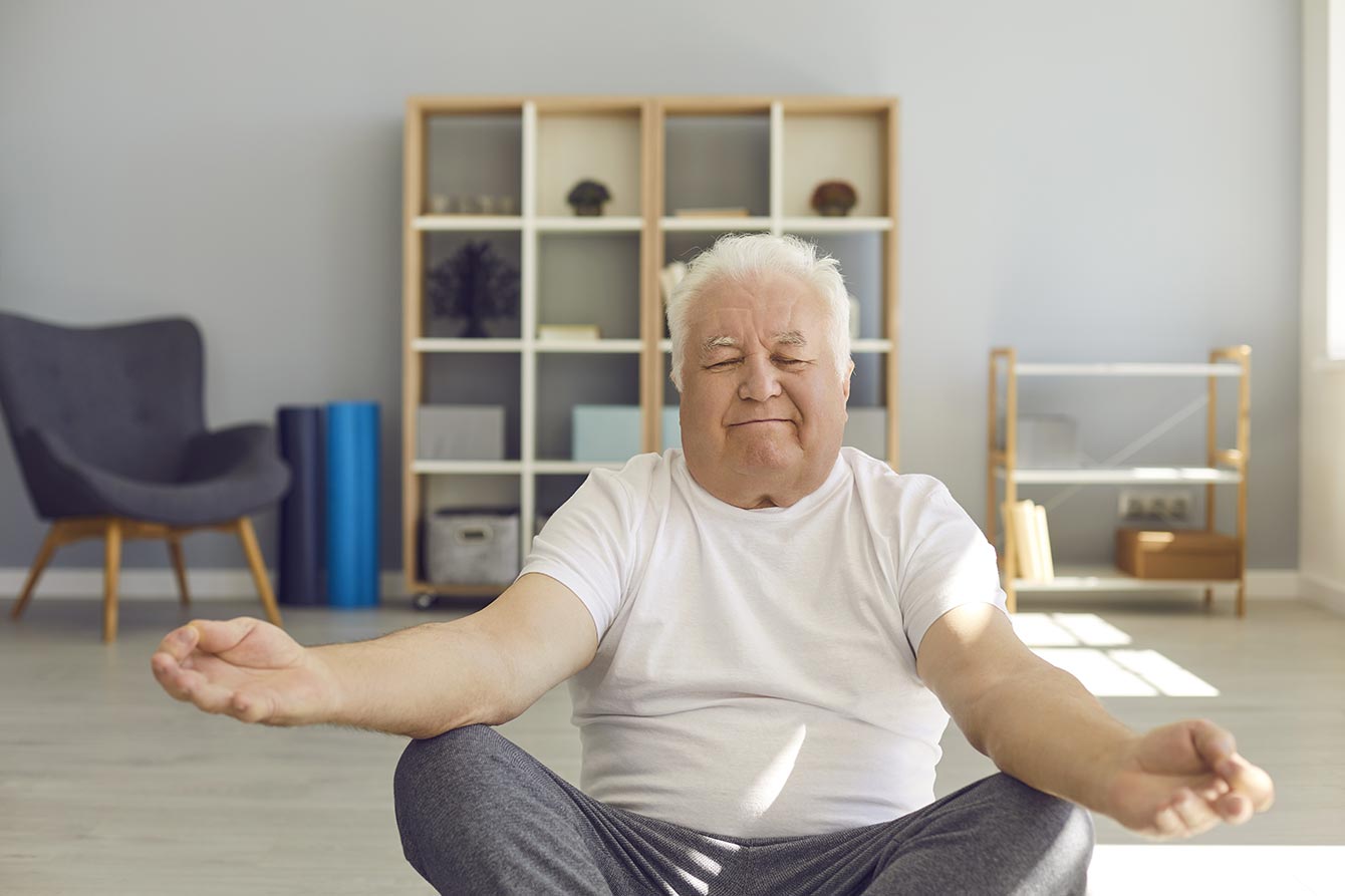 Older man sitting on yoga mat with legs crossed meditating