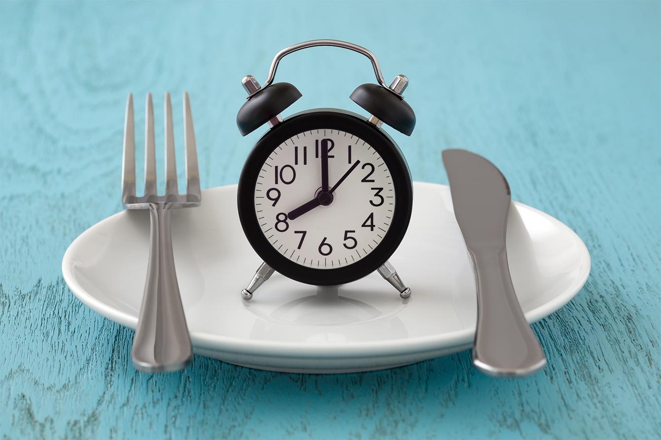 Intermittent fasting and meal planning concept with alarm clock sitting atop empty plate
