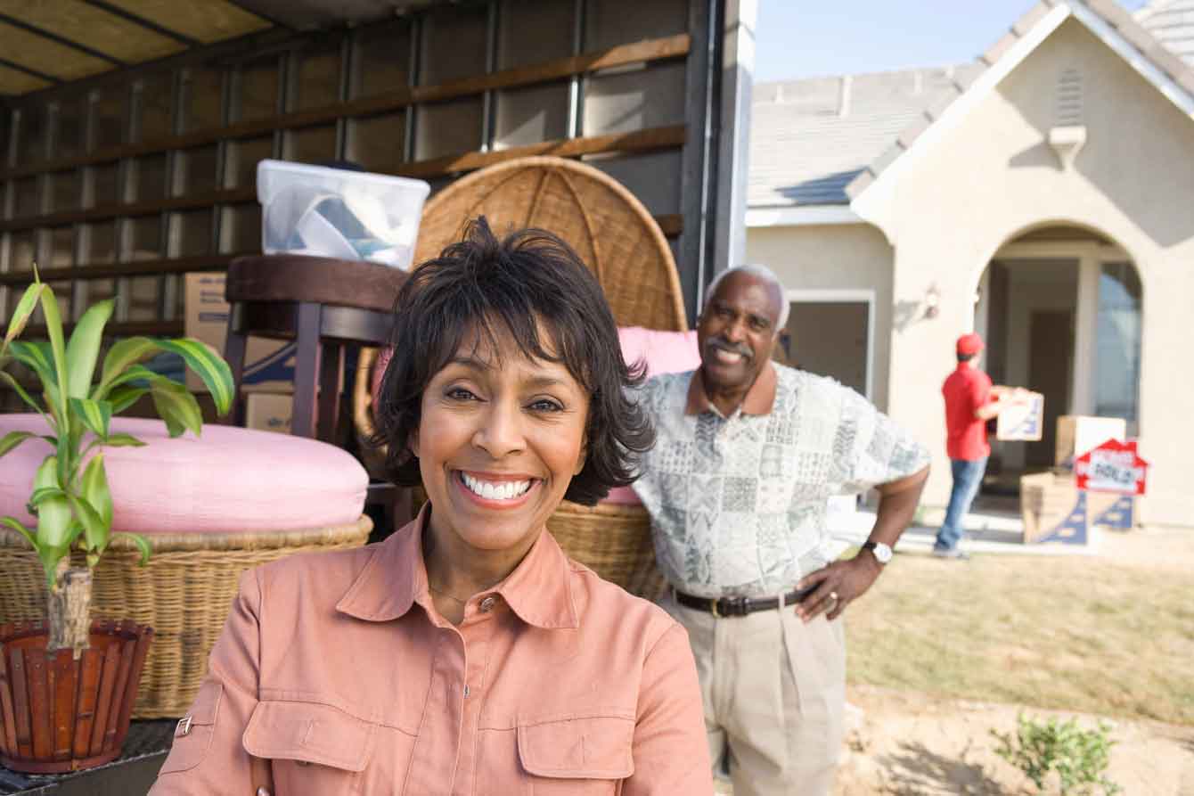 Older black couple carries boxes off of a moving truck