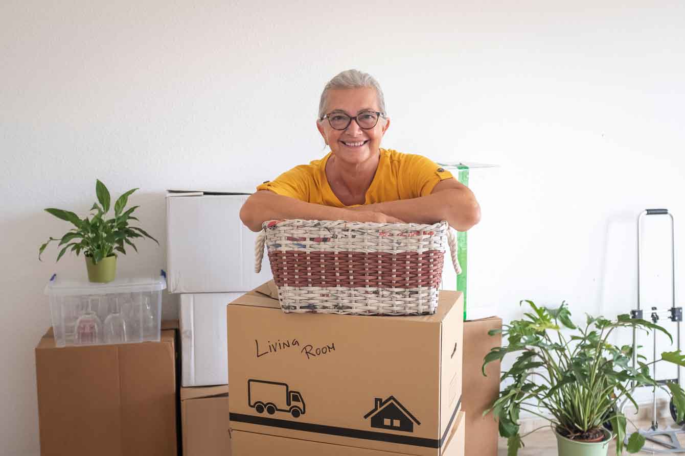 Smiling senior lady stands in front of moving boxes