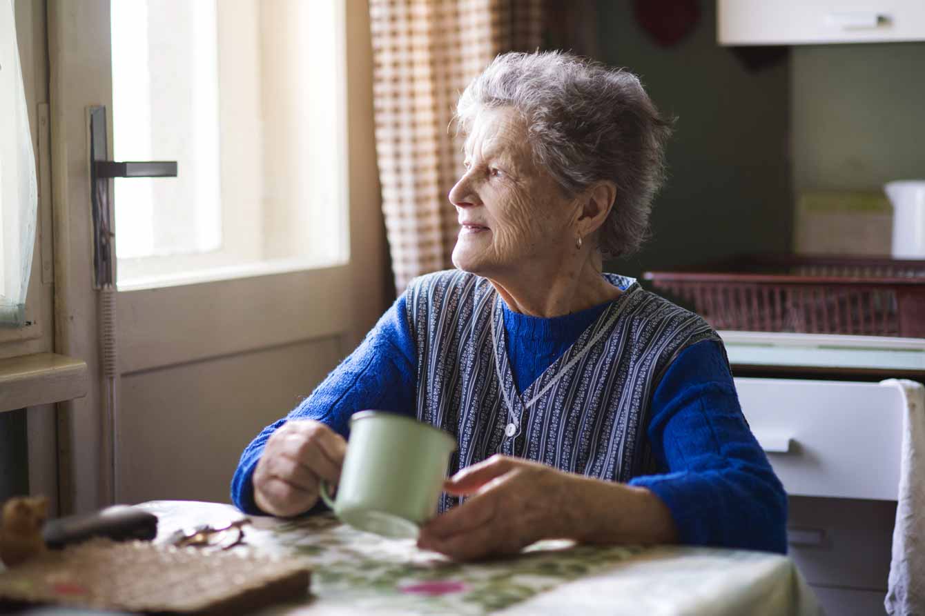 senior woman staring out the window with her nutritional drink