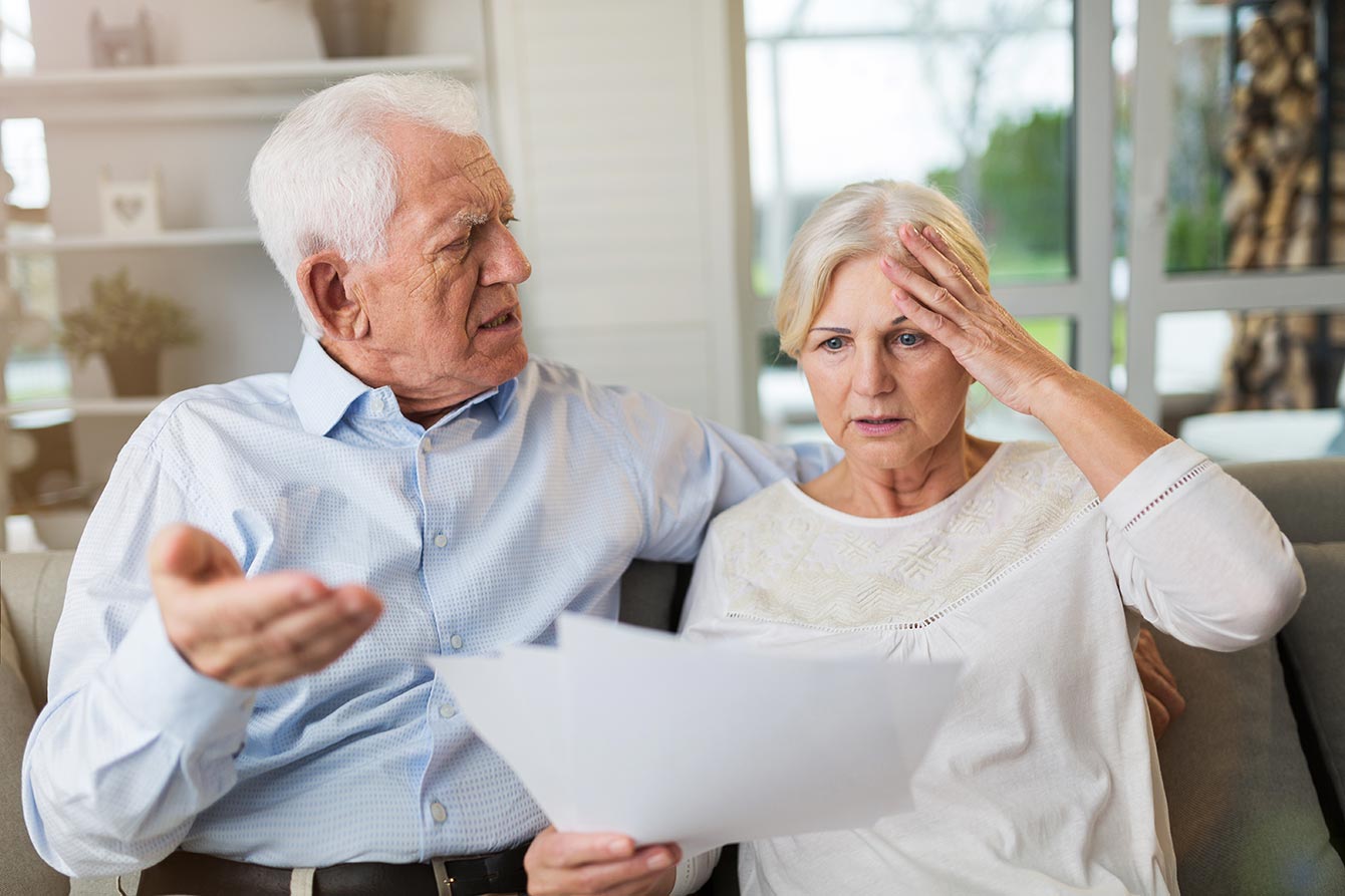 Distraught senior couple sitting on couch looking at paperwork