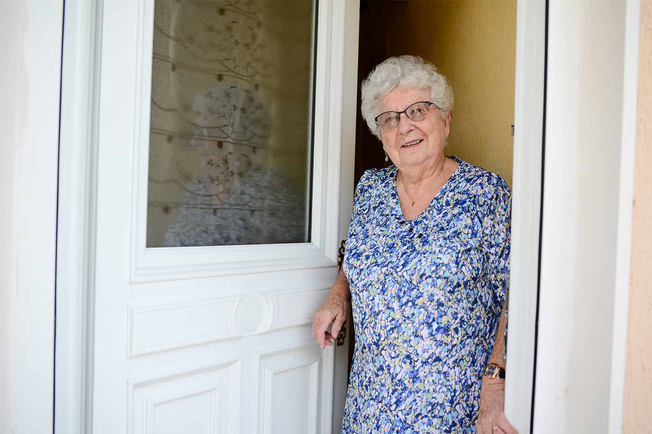 An older woman stands at the front door of her house