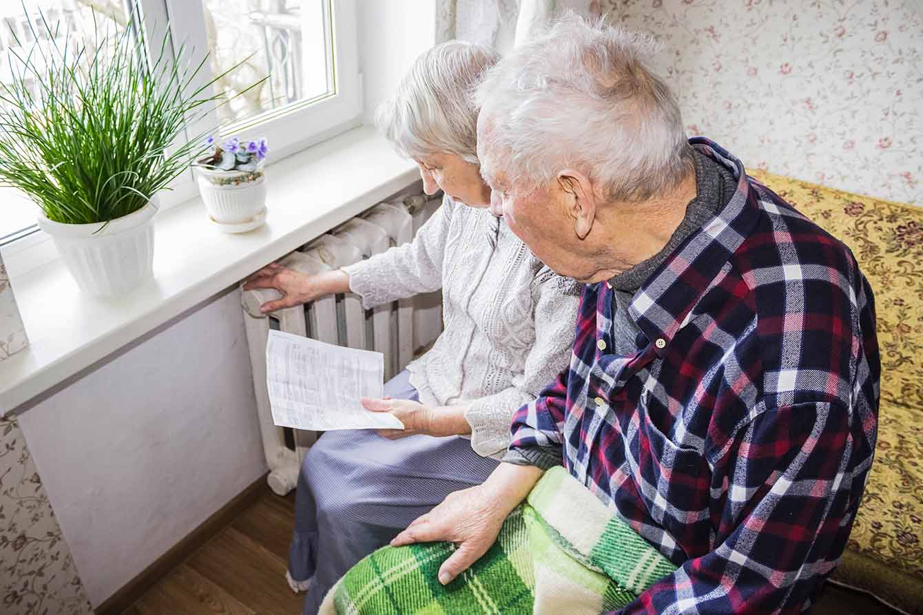 An older couple in front of radiator examine a bill