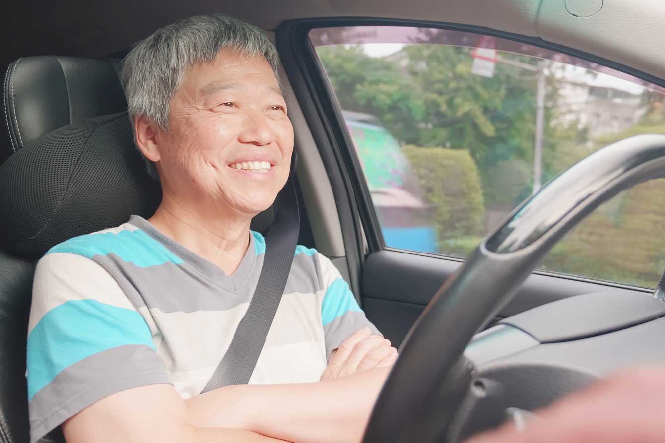 Older asian man smiles in a self-driving vehicle