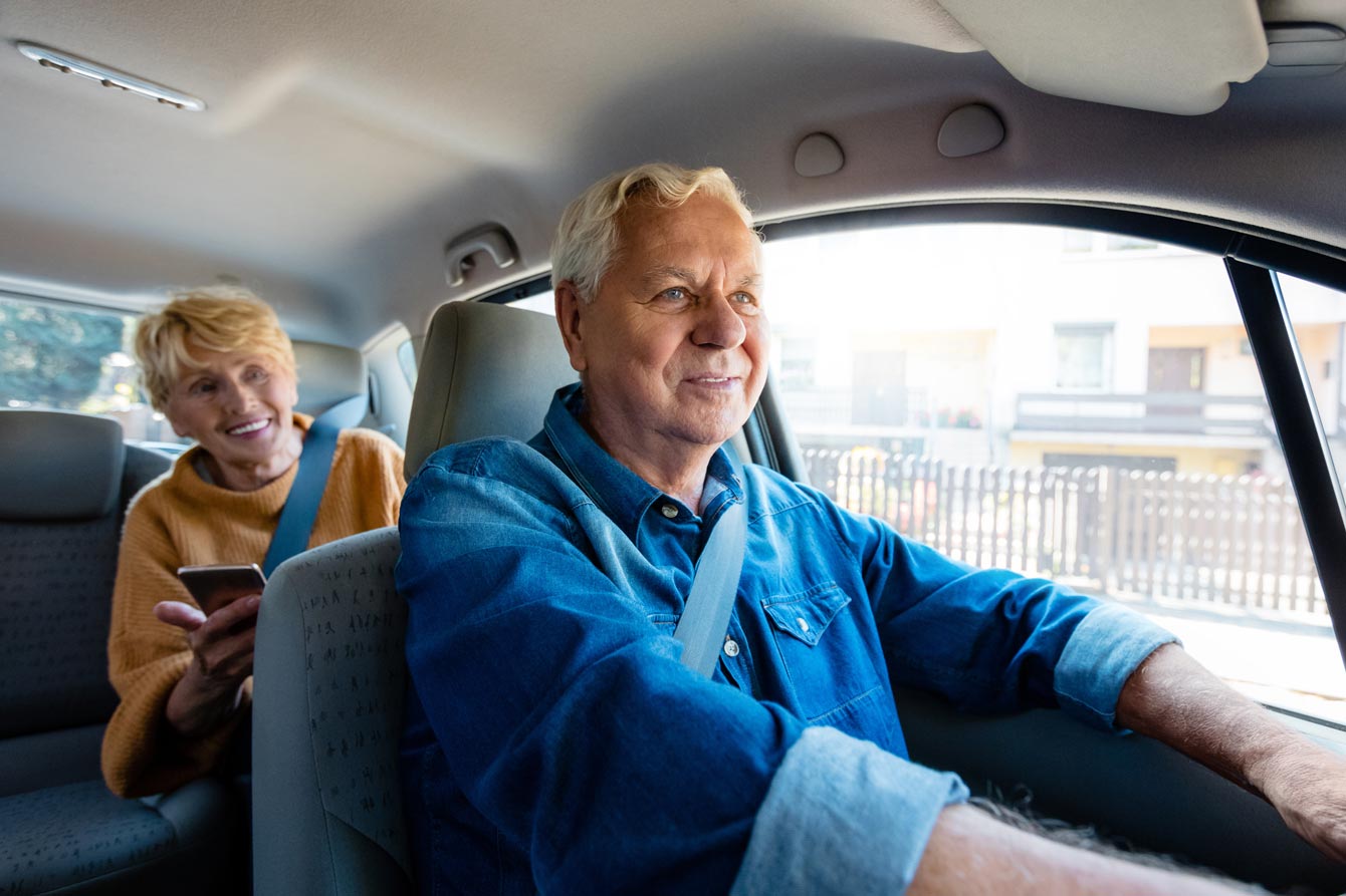 Senior Uber driver sitting in car with older female passenger