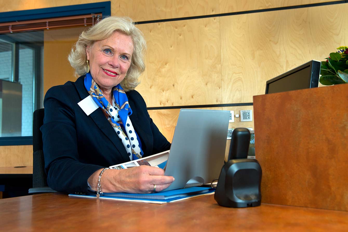 Senior female receptionist sitting behind a desk with computer and phone