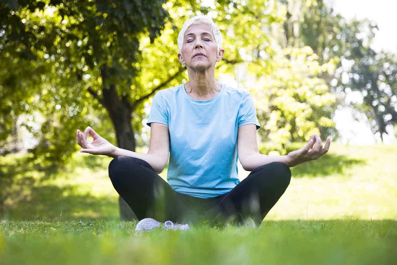 Older woman meditates in a park in the yoga lotus pose position