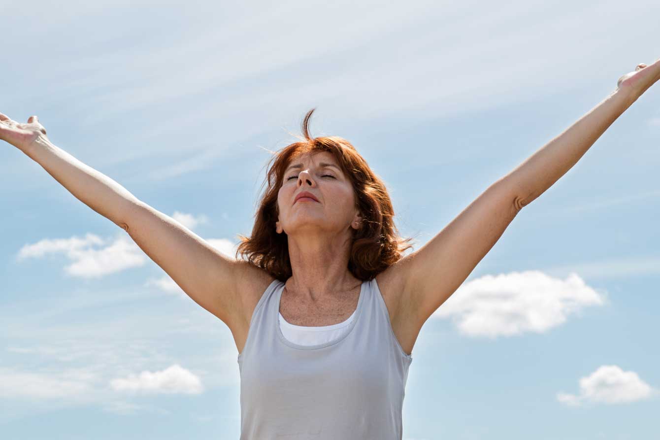 A beautiful older woman opens her arms wide warmed by the sun