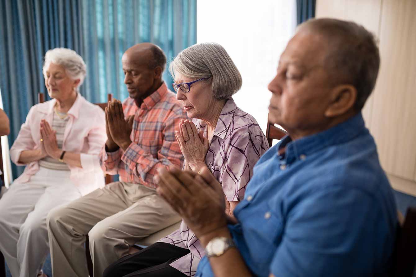 Seniors sitting on chairs while praying together