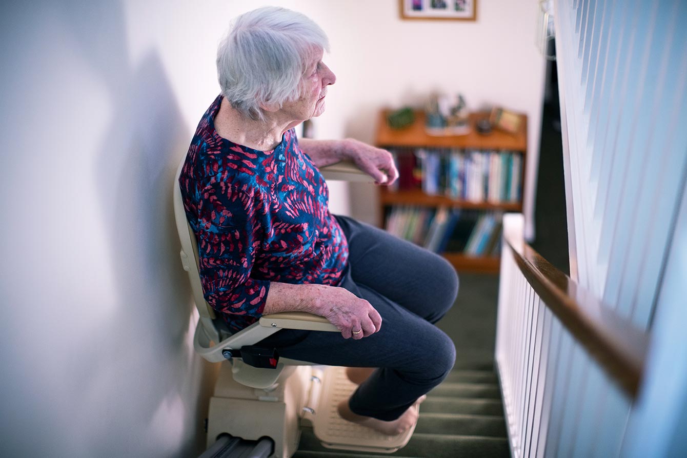 Senior woman sits on a stair lift going up at home