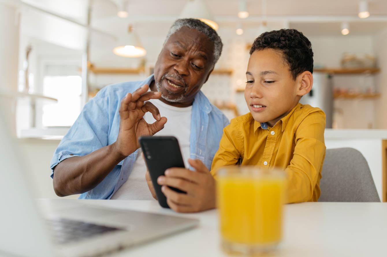 senior grandfather and young grandson sharing a phone on the dining table