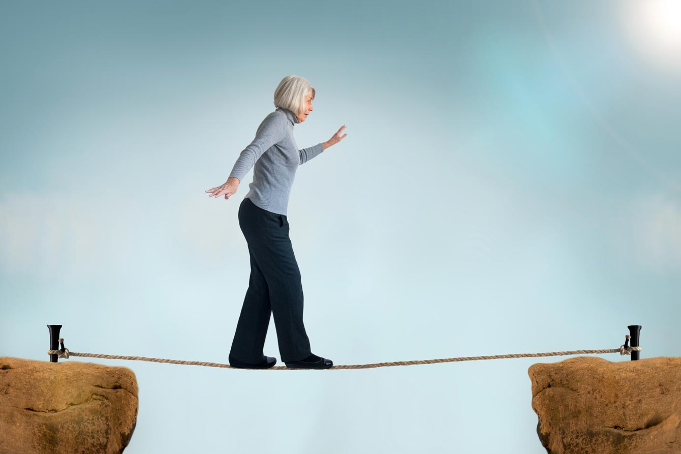 An older woman walks across a tight rope stretched between two boulders