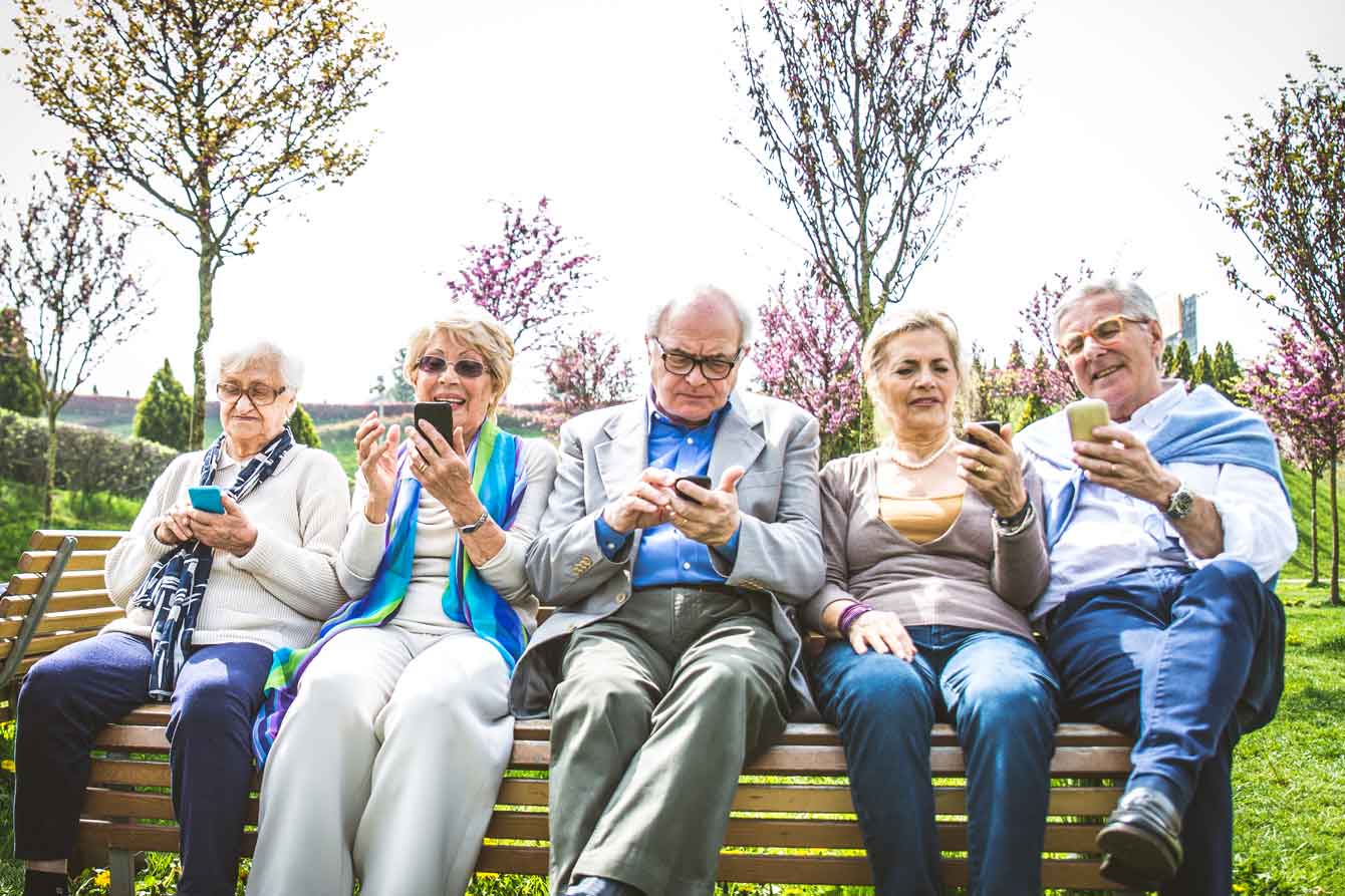 Group of seniors on a bench all looking at their cell phones