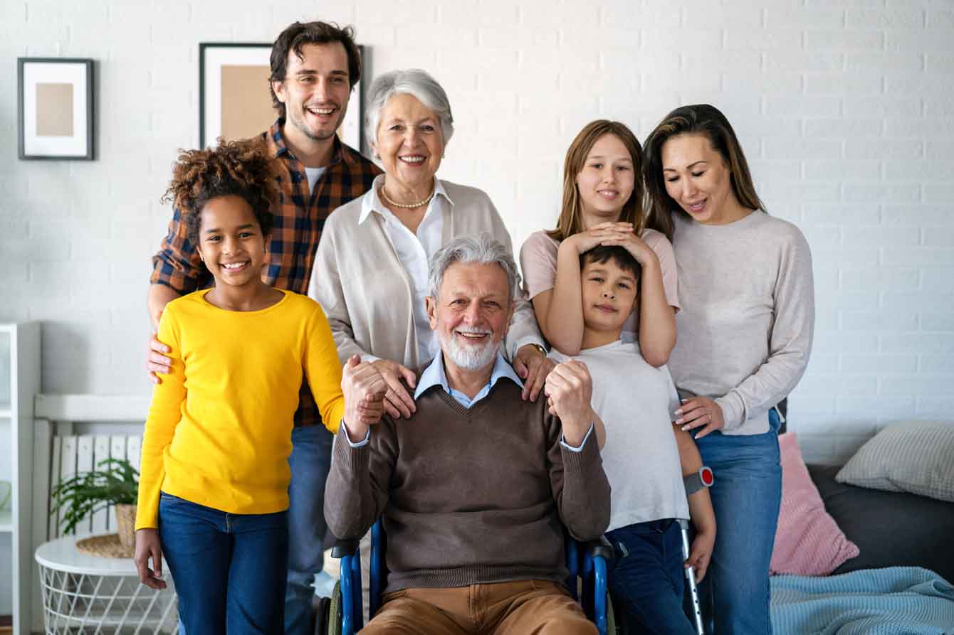 Happy multi generational, multi ethnic family surround older man in wheelchair