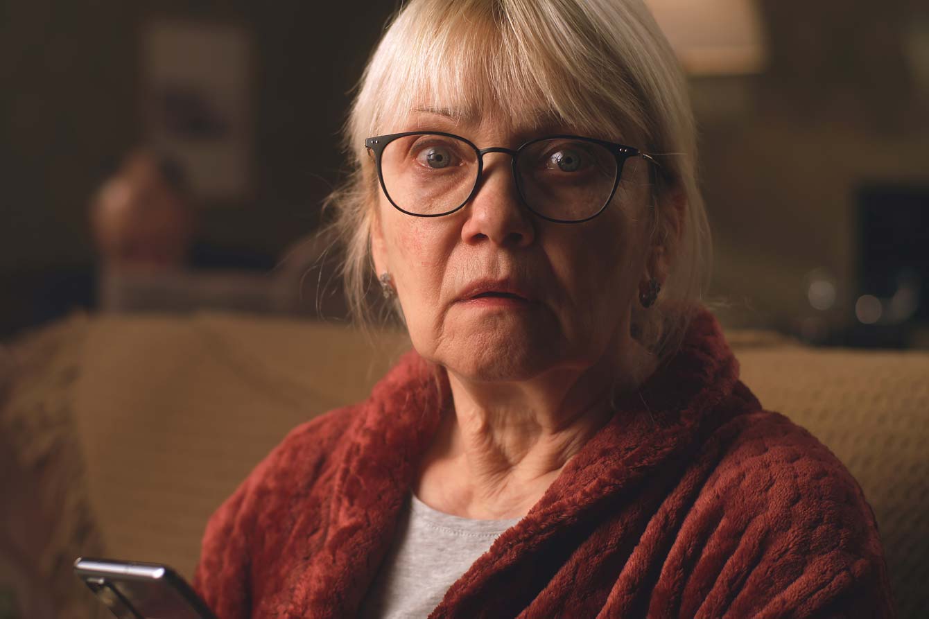A frightened older woman sits on her couch
