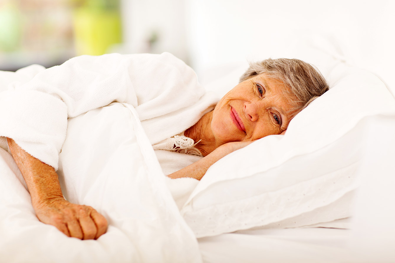 Happy senior woman lying on her side in bed