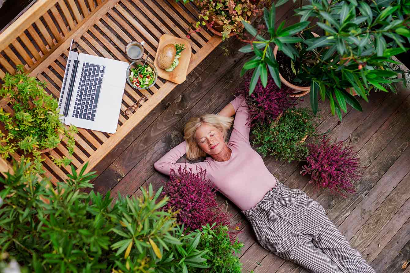 Top view of senior woman with laptop lying outdoors on terrace, resting