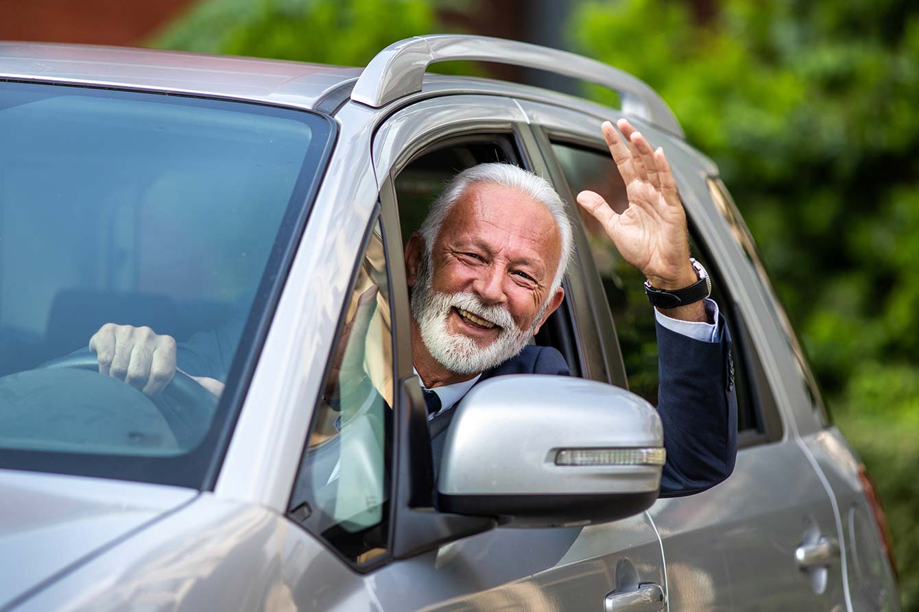 Smiling senior man in suit driving grey car