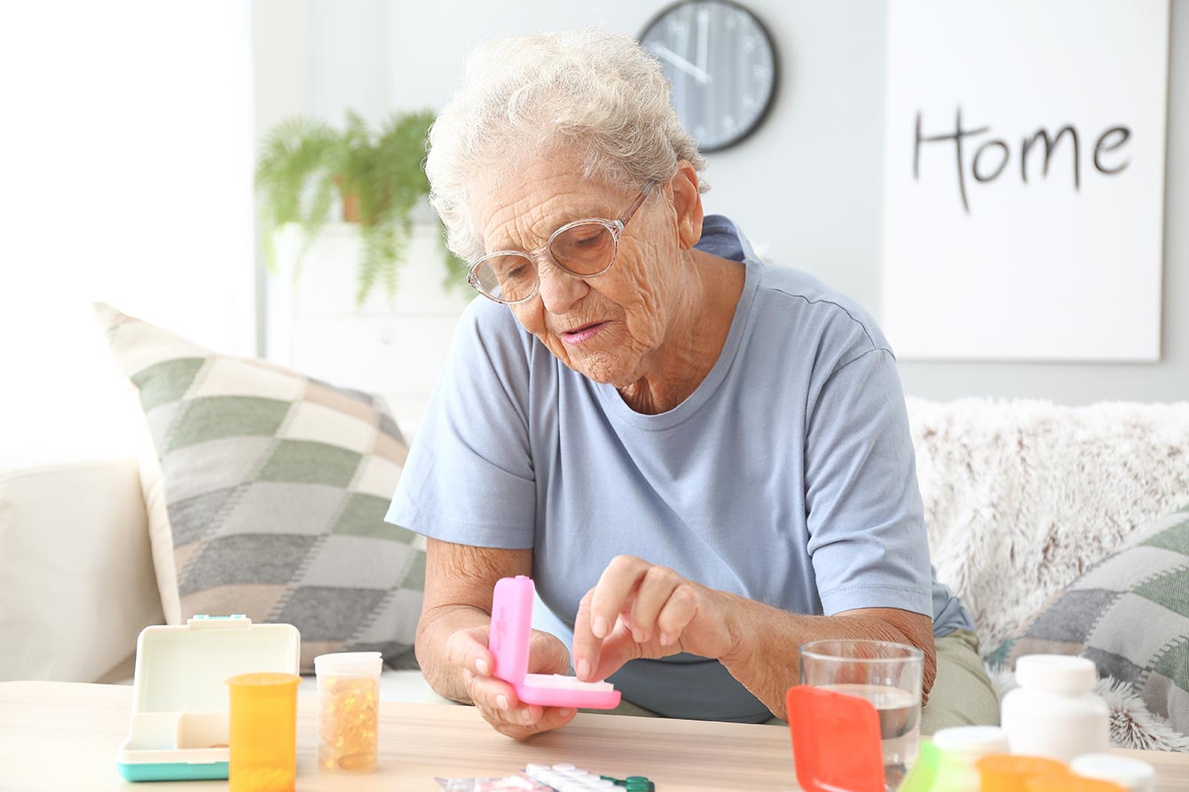 Elderly woman places pills into a pill box at home