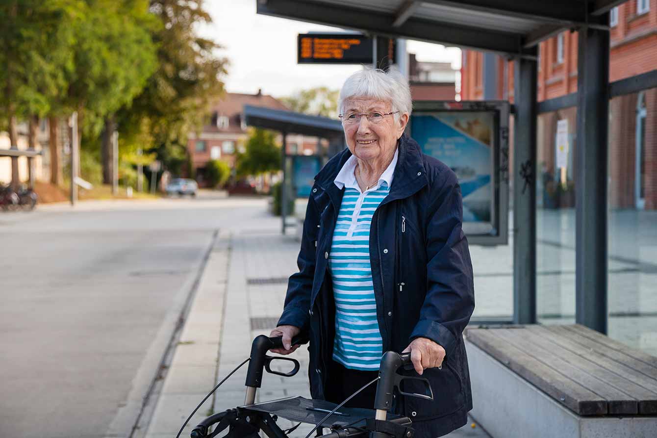 An older lady waits at a bus stop with her walker