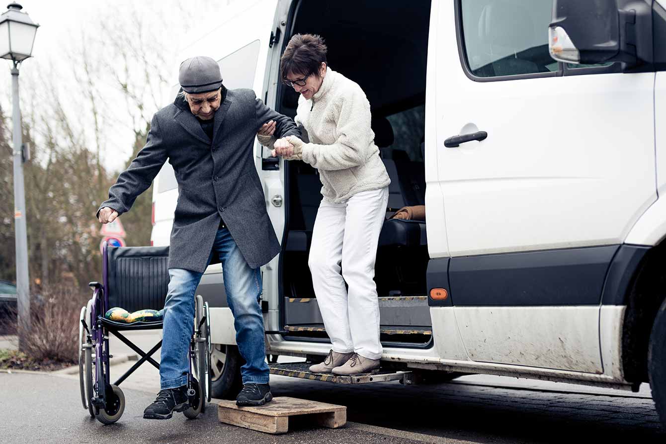 Nurse helps a disabled man to get down from a van
