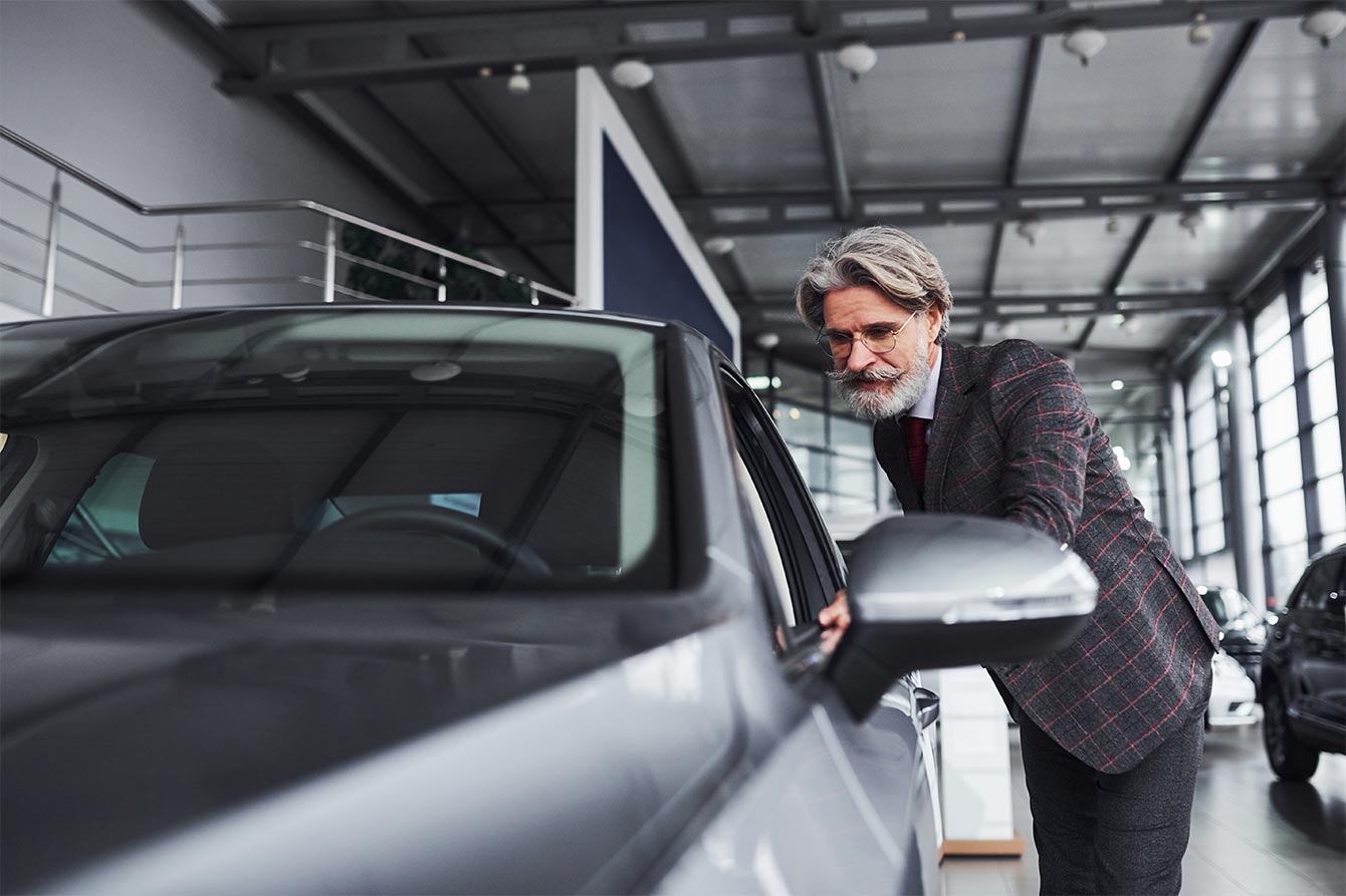 Senior man with mustache shopping for a new gray car in showroom