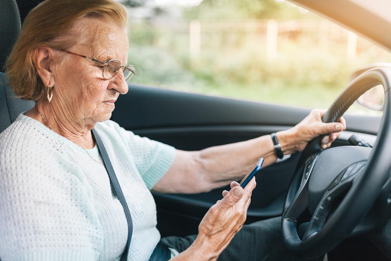 Older woman sits in her car looking at her smart phone