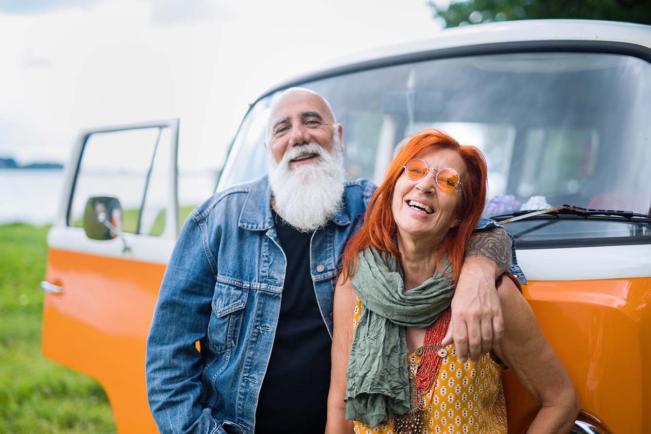 Older hipster couple standing in front of vintage orange van