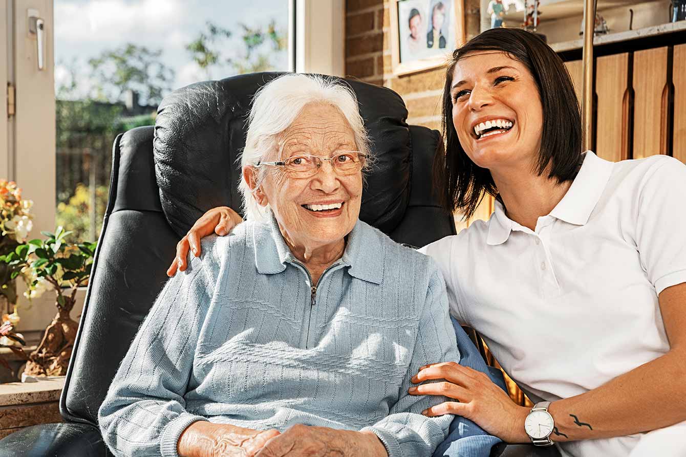 Happy senior woman at home being cared for by a young nurse