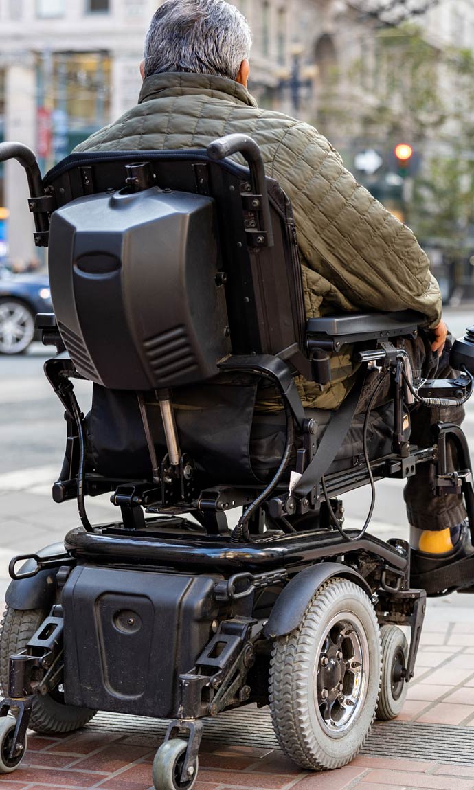 elderly disabled person on an electric wheelchair on a city street in front of a pedestrian crossing.