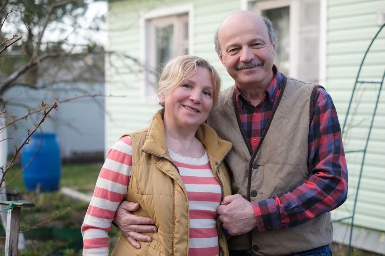 senior couple smiling beside their home