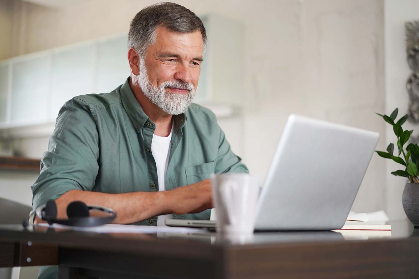 Mature man in casual suit sitting at the table in home office and working at laptop